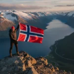 Passa på att besöka Norge En turist viftar med den norska flaggan mot norska fjällen i bakgrund.