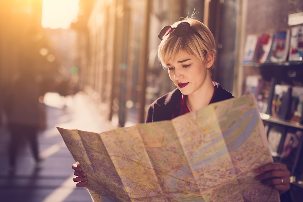 Young beautiful female traveler standing on the street and looking at the map
